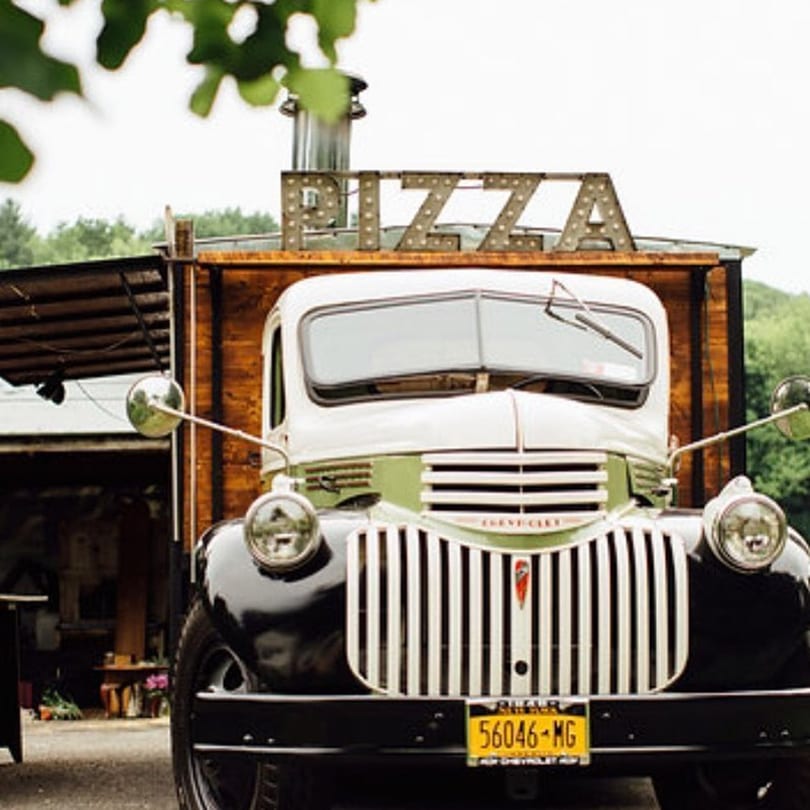A vintage white and green pizza food truck with a "PIZZA" sign on top.
