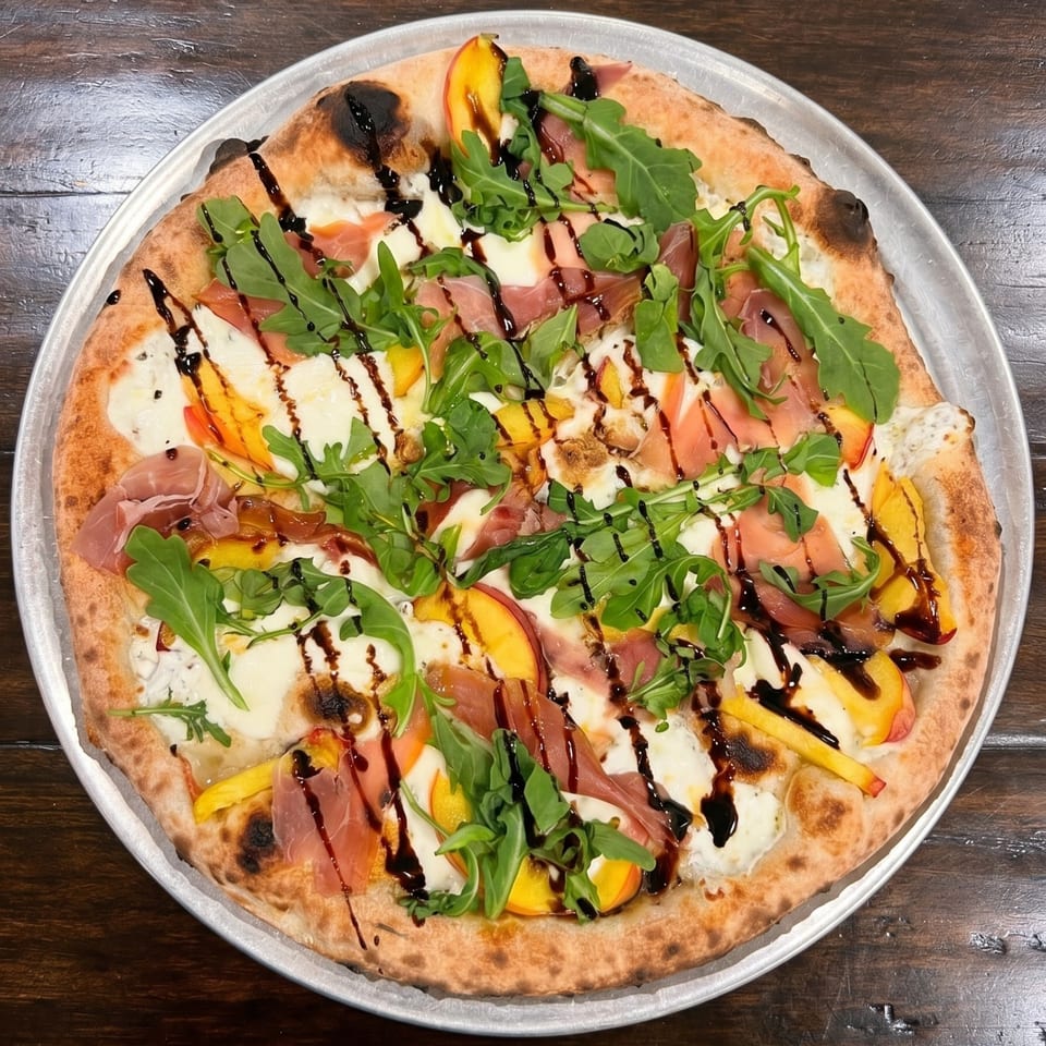 Neapolitan pizza with peaches, prosciutto, arugula, mozzarella, and balsamic glaze on a metal tray.