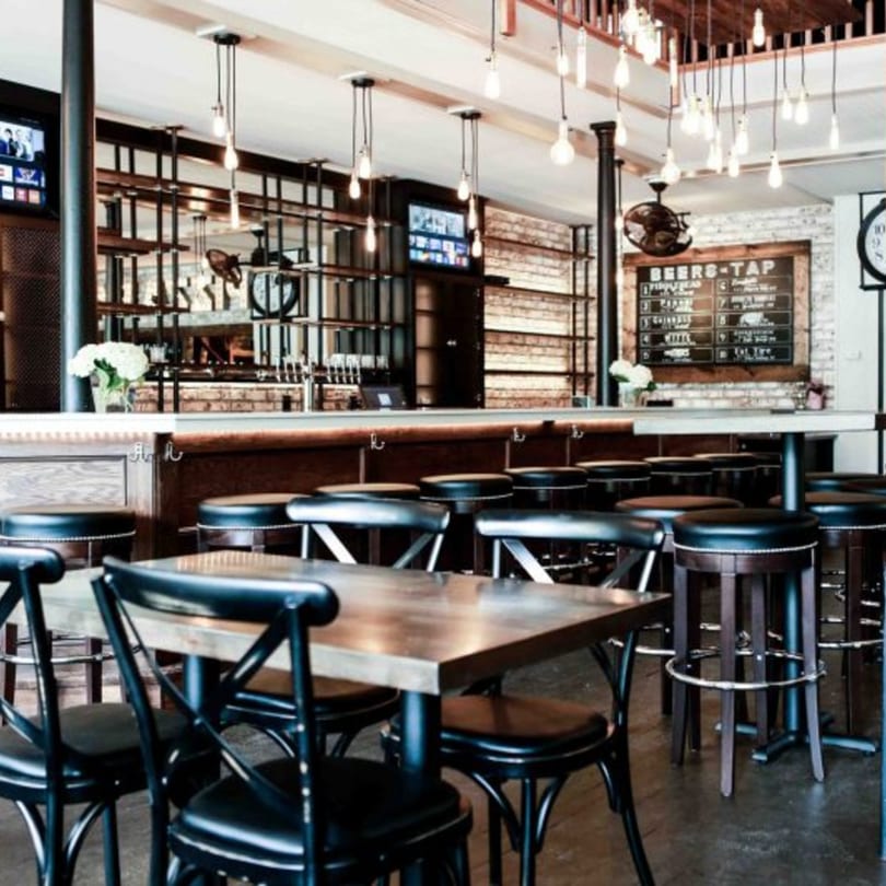 A cozy restaurant interior with wooden tables, black chairs, and a bar with stools.