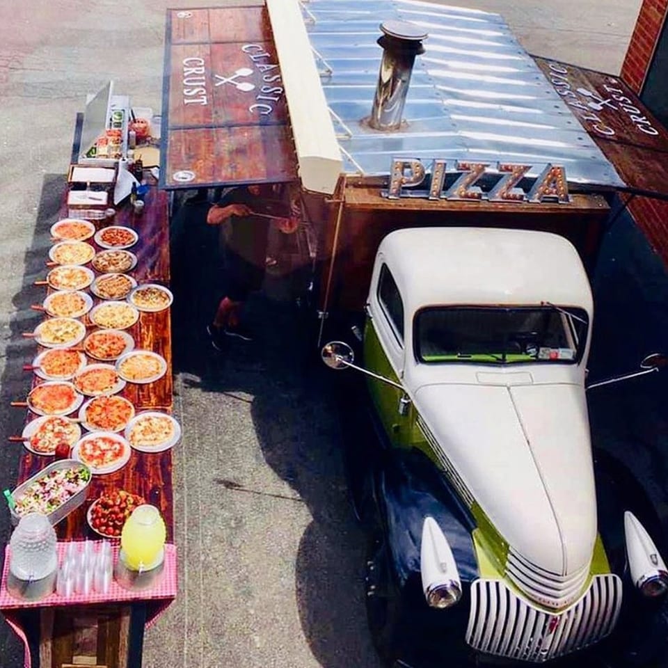 Overhead view of a Classic Crust pizza truck and a table laden with pizzas and drinks.