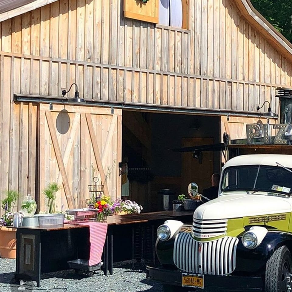 A rustic wooden barn with open doors revealing a food truck and outdoor serving station.