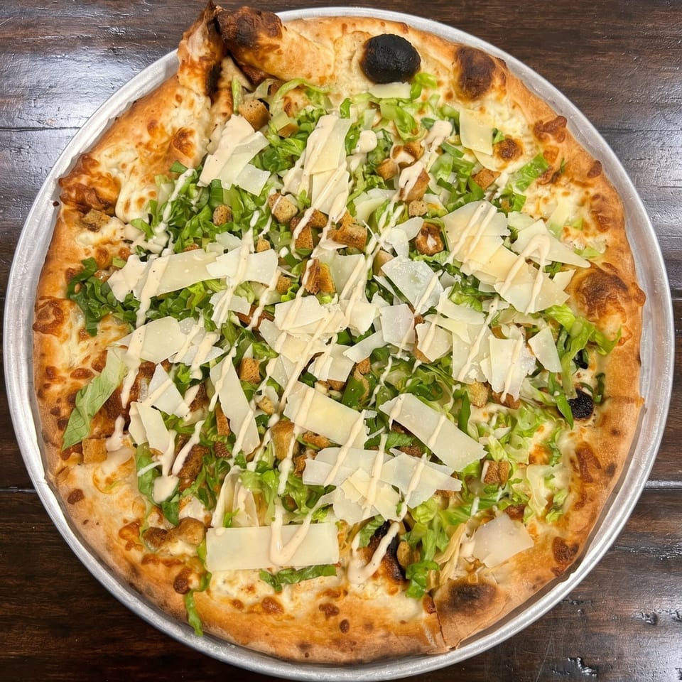 Caesar salad pizza with romaine lettuce, croutons, parmesan, and dressing on a metal tray.