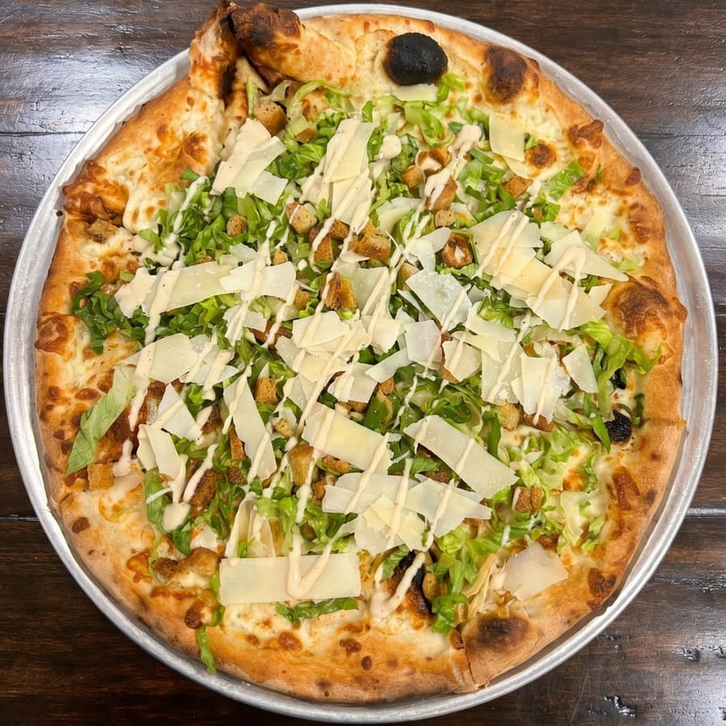 A whole Caesar salad pizza, topped with lettuce, croutons, parmesan, and dressing.