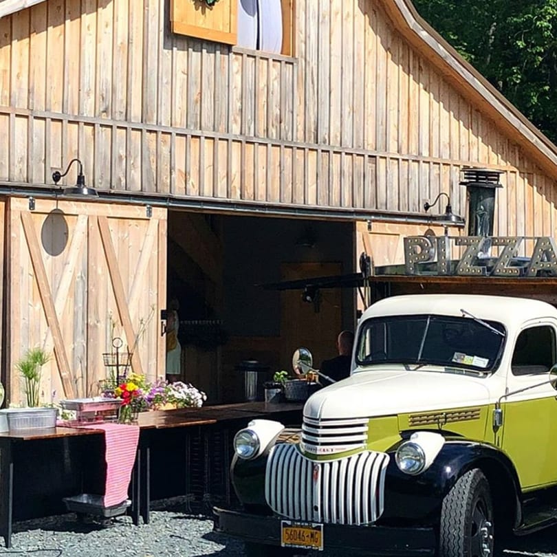 A vintage white and lime green pizza truck parked in front of a rustic wooden barn.