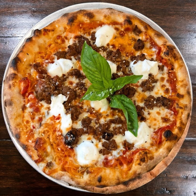 A whole pizza with crumbled sausage, dollops of ricotta, and fresh basil on a metal pan.