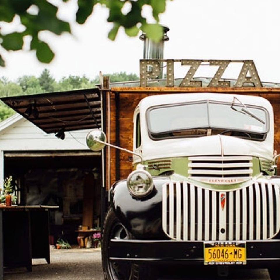 Vintage white and green pizza food truck with a "PIZZA" sign on top.